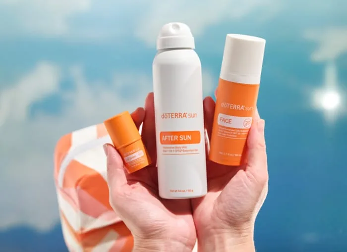 La brume après-soleil, l'écran visage et le stick dōTERRA sun tenus en mains devant un ciel d'été
